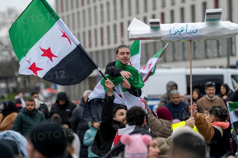 People celebrate the end of the Assad regime after the change of power in Syria at a rally on the square in front of the main railway station in Duisburg, North Rhine-Westphalia, Germany, Europe