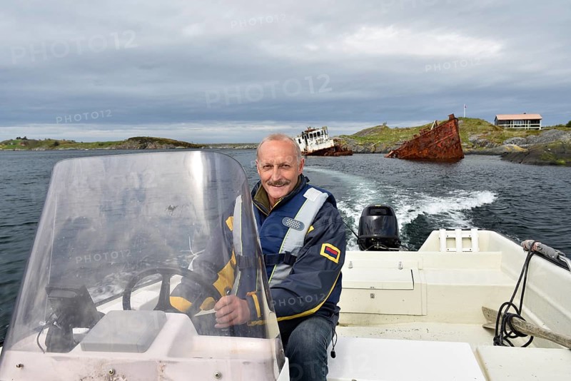 Man, senior driving motorboat, fishing boat at a shipwreck on the Atlantic Road in Norway