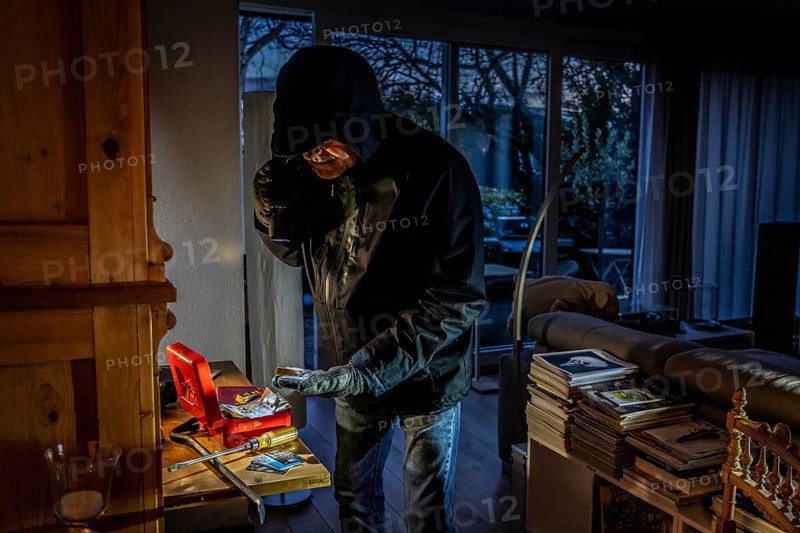 Symbolic image of a burglary, perpetrator has broken into a flat from the garden side and is looking for loot, breaks open a cash box, finds valuables, money