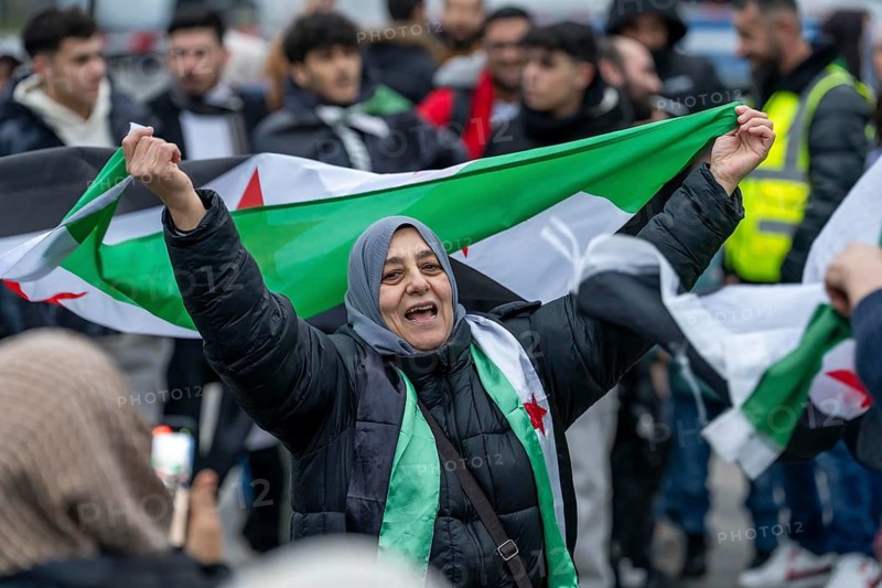 Syrian woman celebrate the end of the Assad regime after the change of power in Syria at a rally on the square in front of the main railway station in Duisburg, North Rhine-Westphalia, Germany, Europe