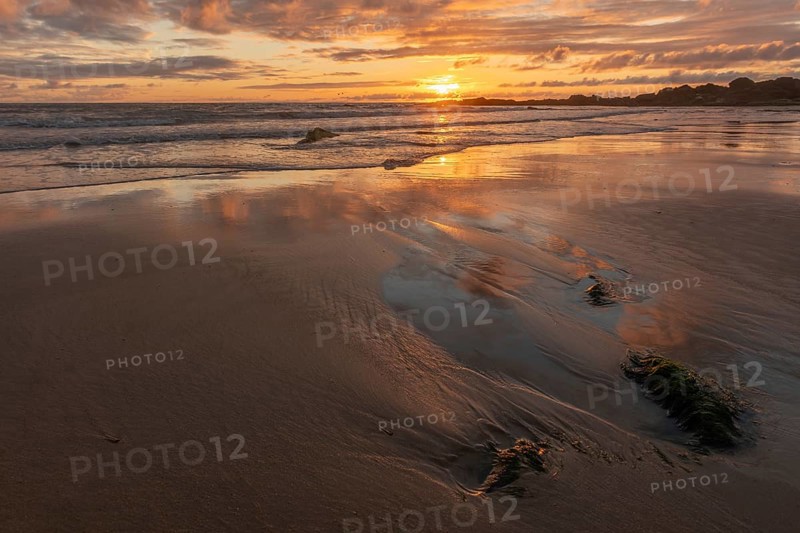 A beach with a rock and a sunset, the sky is reflected on the sand of a beach. The sky is cloudy and the sun is out. Les Sables d'Olonne, Vendee, France, Europe