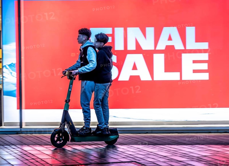 2 teenagers on an e-scooter, final sale, clothing department stores' on Schadowstraße, large poster in the shop window advertising the winter sale, rainy weather, Düsseldorf, North Rhine-Westphalia, Germany, Europe