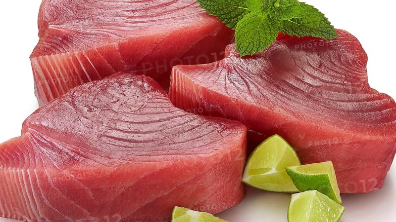 3 slices of raw tuna (thunnus), decorated with pieces of lime and mint leaves, studio shot
