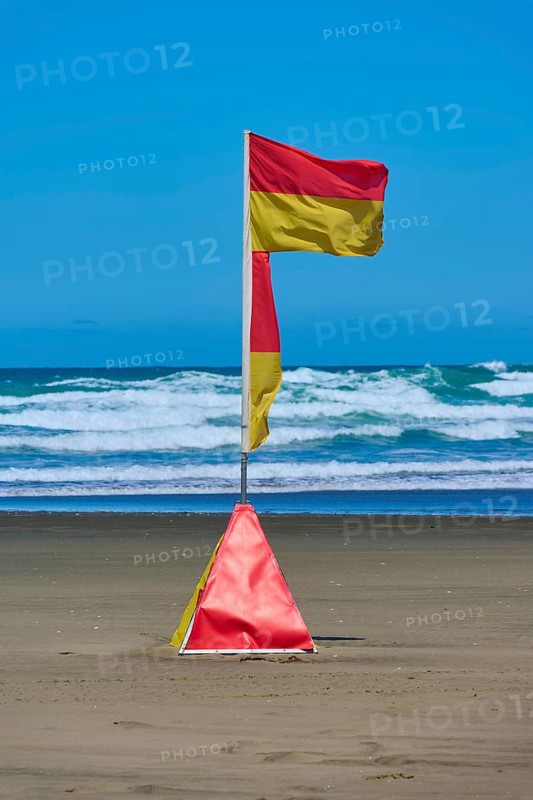 A red and yellow coastguard banner on the beach against a backdrop of waves under a clear blue sky, Bethells Beach, Te Henga, Auckland, New Zealand, Oceania