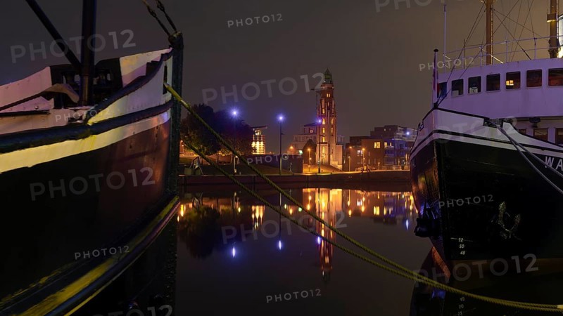 View over the new harbour to the Simon Loschen lighthouse through two moored ships in Bremerhaven at night, Bremerhaven, Bremen, Germany, Europe