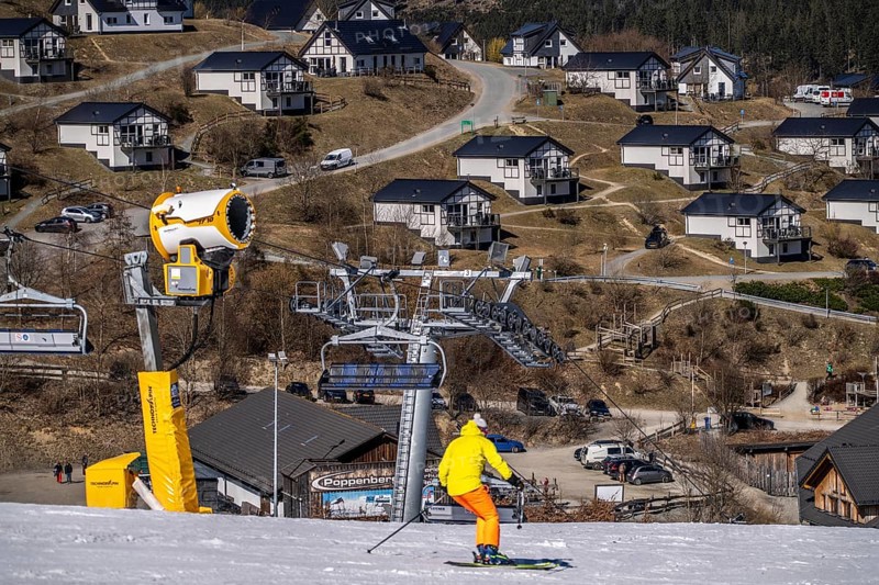 Winter sports area in the Sauerland, Winterberg ski lift carousel, artificial snow slopes, artificial snow from over 360 snow guns, Poppenberg ski area, 12 of 24 lifts are in operation in mid-March, the rest of the landscape is snow-free, in the background holiday homes at Landal Ferienpark Winterberg, North Rhine-Westphalia, Germany, Europe