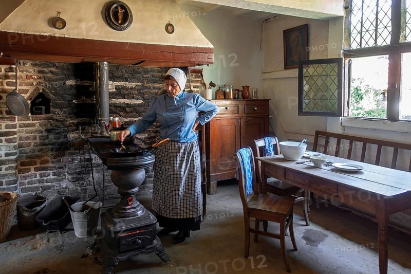 Old woman cooking on antique Flemish cast-iron coal stove, Leuvense stoof in 19th century house, open air museum Bokrijk, Limburg, Flanders, Belgium, Europe