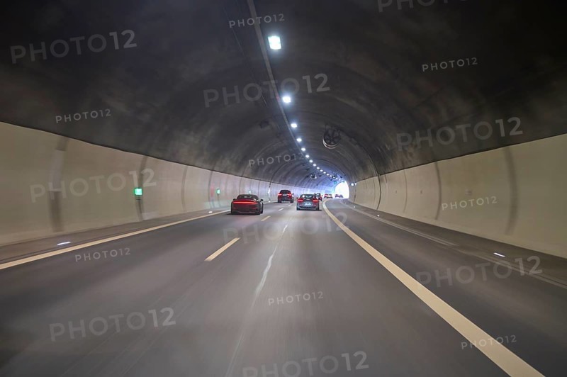 Motorway tunnel with several cars, illuminated by overhead lights, Switzerland, Europe