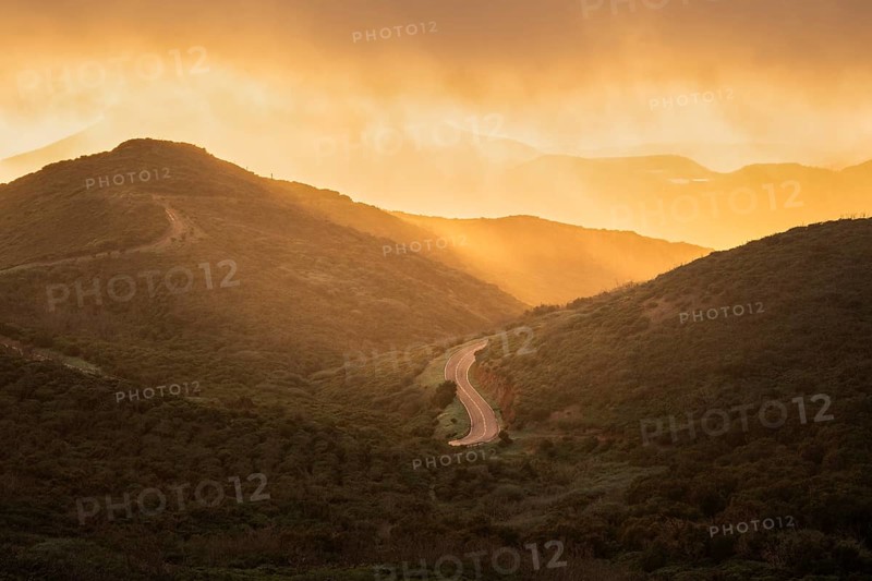 View from a path below the summit of Garajonay to other mountains of the Garajonay National Park and a road. After a rain shower, with sun and golden hour with bright clouds. Parque Nacional de Garajonay, La Gomera, Canary Islands, Spain, Europe