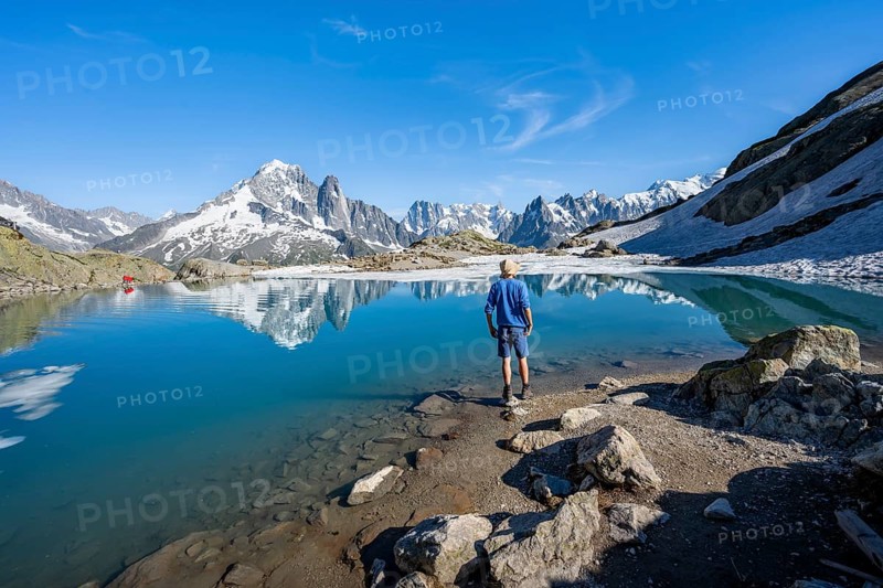 Mountaineer in front of mountain landscape with mountain lake, tourist at Lac Blanc with water reflection, mountain peak Aiguille Verte, Grandes Jorasses, Aiguille du Moine and Mont Blanc, Mont Blanc massif, Chamonix-Mont-Blanc, Haute-Savoie, France, Europe