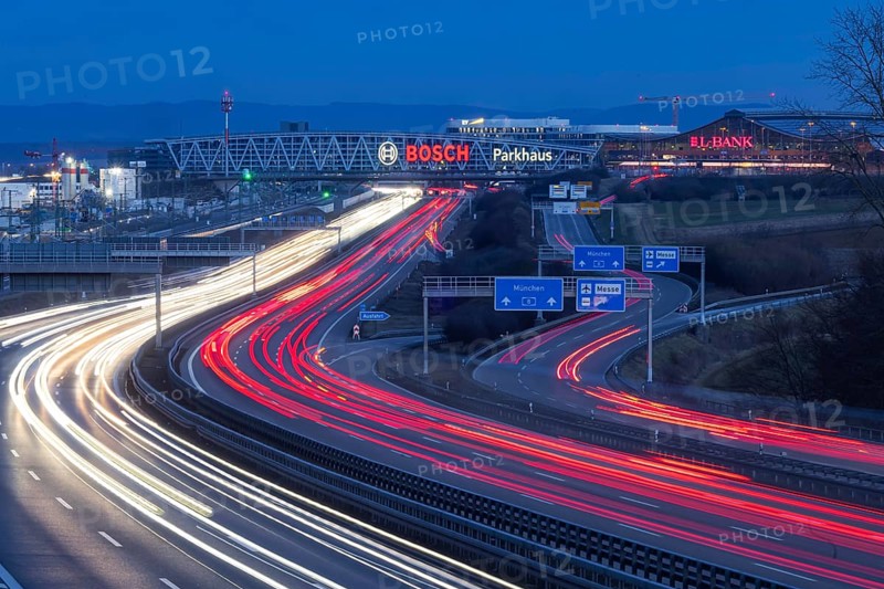 A8 motorway at Stuttgart Airport in the evening. Heavy traffic, lanes of light. Modern architecture of Messe Stuttgart with multi-storey car park above the motorway lanes. Logo of the Bosch company. Stuttgart, Baden-Württemberg, Germany, Europe