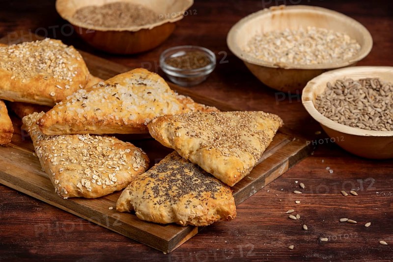 Freshly baked dough triangles sprinkled with sunflower seeds, poppy seeds, sesame seeds, oat flakes and salt on a wooden board
