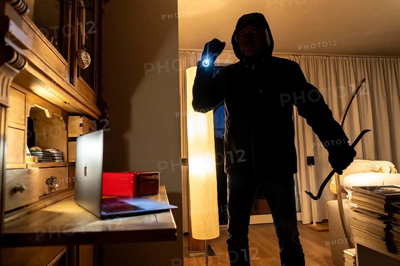 Symbolic image of a burglary, perpetrator has broken into a flat from the garden side and is looking for loot, computer, laptop, valuables, money, technology