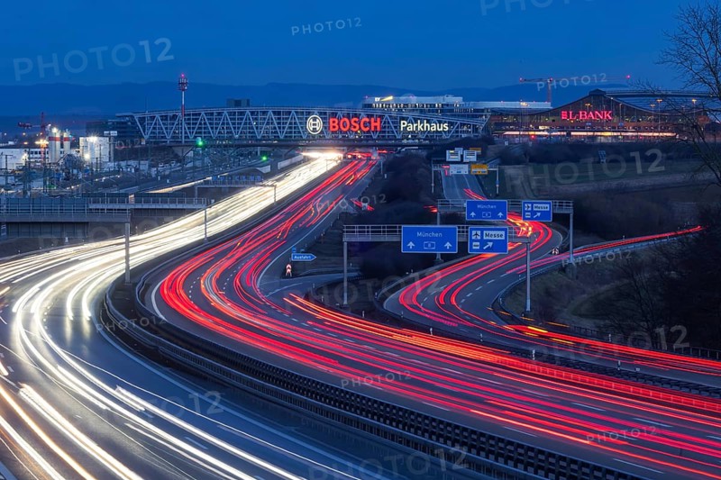 A8 motorway at Stuttgart Airport in the evening. Heavy traffic, lanes of light. Modern architecture of Messe Stuttgart with multi-storey car park above the motorway lanes. Logo of the Bosch company. Stuttgart, Baden-Württemberg, Germany, Europe