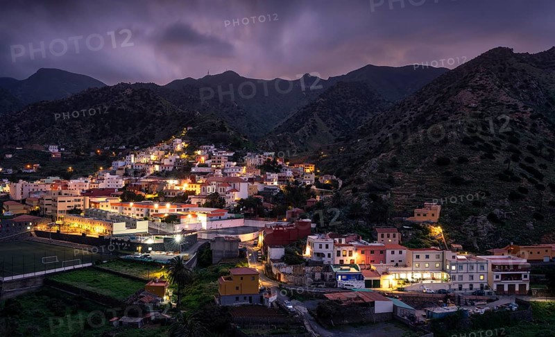 View of Vallehermoso and the surrounding mountain landscape at dusk under a cloudy sky. The street lights are switched on. Vallehermoso, La Gomera, Canary Islands, Spain, Europe
