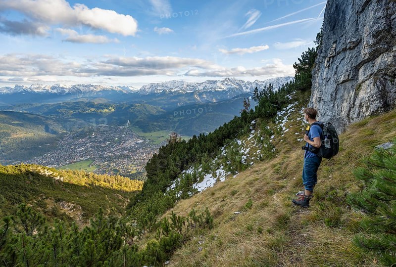 Mountaineer on a narrow hiking trail between mountain pines, view of Garmisch-Partenkirchen and mountain panorama, hike to Kramerspitz, in autumn, Ammergau Alps, in autumn, Bavarian Alps, Bavaria, Germany, Europe
