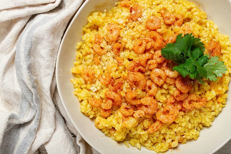 Risotto with shrimp, in a bowl, on a textured surface, with a side dish of fresh coriander, homemade, no people