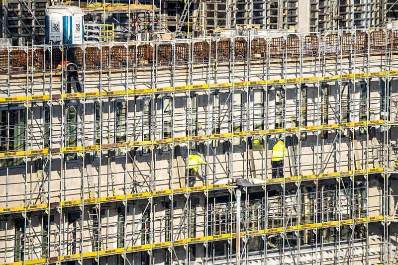 Large construction site, scaffolded new building, factory and office building, workers on the scaffolding during facade work