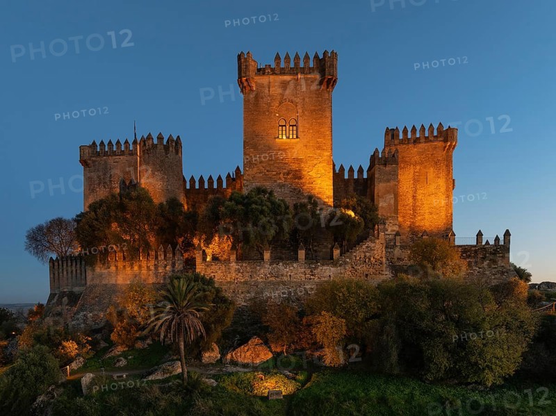 The impressive eighth-century Moorish castle of Almodóvar del Río perches high above the Guadalquivir river valley. Floodlit at dusk. Drone shot. Córdoba province, Andalusia, Spain, Europe