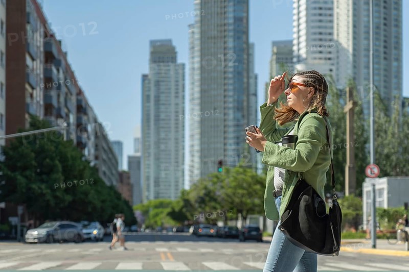 Young businesswoman crossing the street holding a coffee and protecting herself from the sun in puerto madero, a modern neighborhood and popular tourist destination in buenos aires, argentina