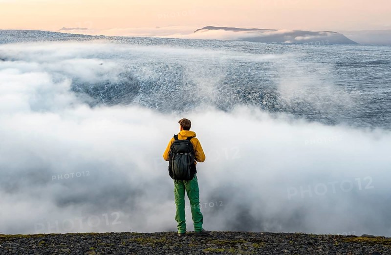 Young man in front of impressive landscape at sunset, fog, clouds moving around, glacier ice of the glacier tongue Kötlujökull, glacier Myrdalsjökull, Pakgil, Iceland, Europe