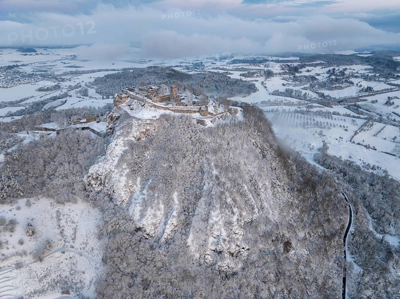 Aerial view of the snow-covered Hegau volcano Hohentwiel with Germany's largest castle ruins on a cold winter morning, in front of sunrise, surrounded by frosty trees in a winter landscape, district of Constance, Baden-Württemberg, Germany, Europe