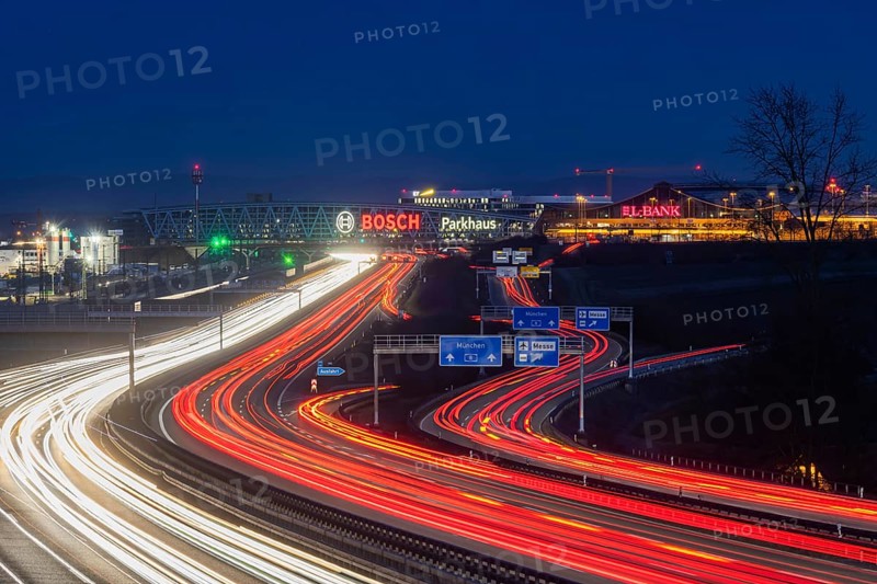 A8 motorway at Stuttgart Airport in the evening. Heavy traffic, lanes of light. Modern architecture of Messe Stuttgart with multi-storey car park above the motorway lanes. Logo of the Bosch company. Stuttgart, Baden-Württemberg, Germany, Europe