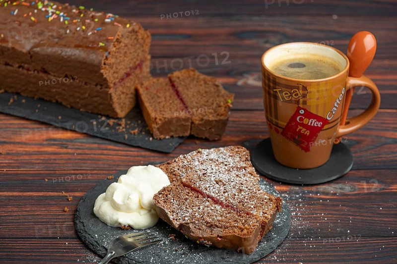 Chocolate cake, pieces with icing sugar and whipped cream, next to a cup of coffee
