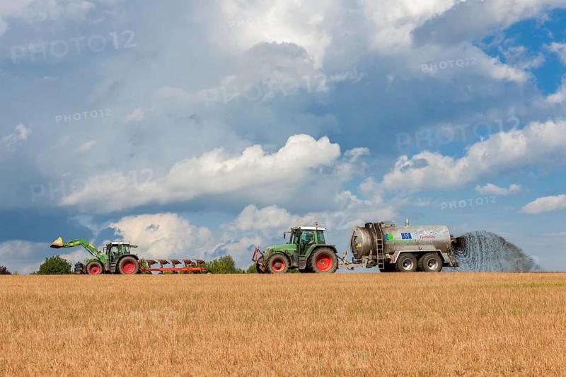 Two tractors in a field with a fertiliser spreader under a cloudy sky, Baden-Württemberg, Germany, Europe
