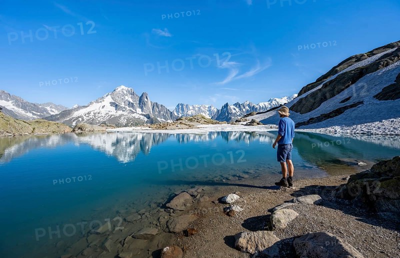 Mountaineer in front of mountain landscape with mountain lake, tourist at Lac Blanc with water reflection, mountain peak Aiguille Verte, Grandes Jorasses, Aiguille du Moine and Mont Blanc, Mont Blanc massif, Chamonix-Mont-Blanc, Haute-Savoie, France, Europe