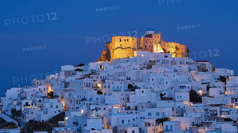 An illuminated fortress towers above white-washed buildings under a deep blue night sky, Querini Castle, Chora, Astypalea, Dodecanese, Greek Islands, Greece, Europe