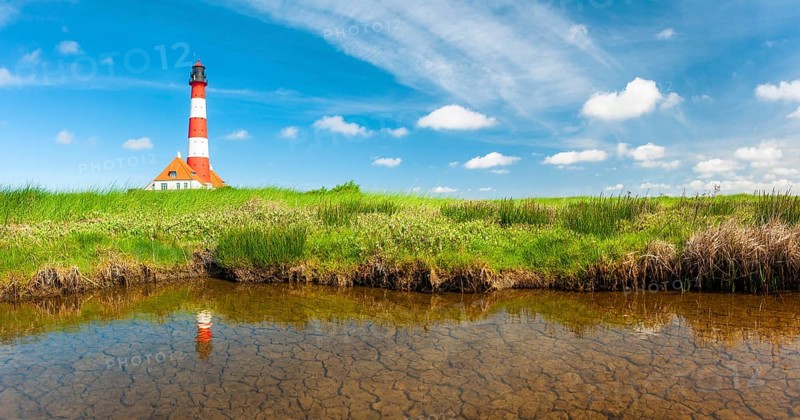 The Westerheversand lighthouse under a blue sky with white clouds reflected in a tideway, Westerhever, Eiderstedt peninsula, Schleswig-Holstein, Germany, Europe
