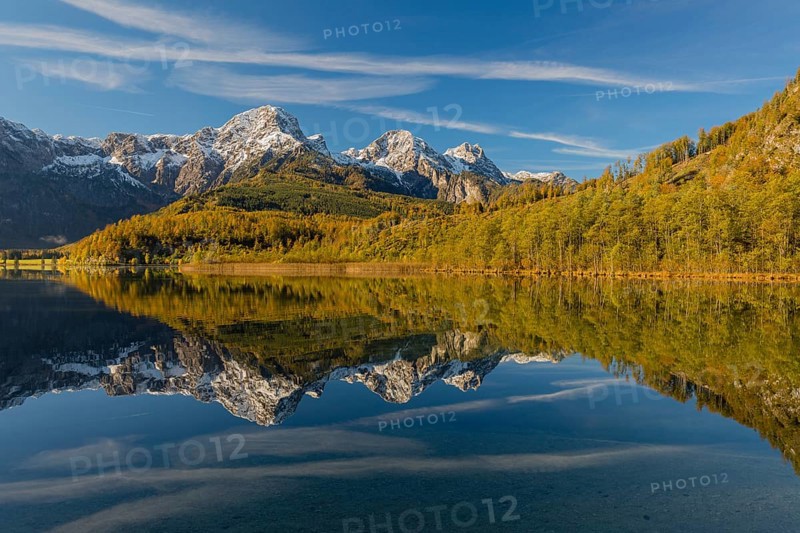 Lake Almsee in autumn with mountains reflected in the lake. Blue sky