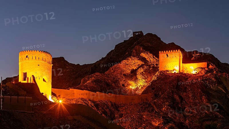 Illuminated city wall with watchtowers at dawn at the Sultan's Palace, Muscat, Arabian Peninsula, Sultanate of Oman