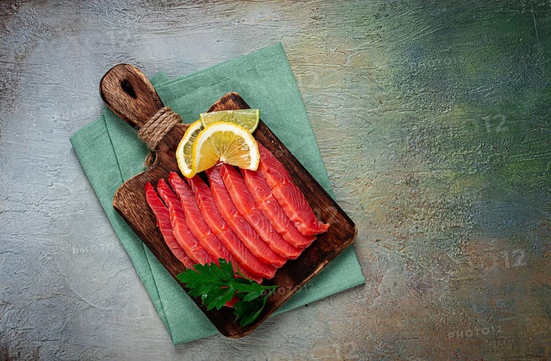 Chum salmon, cold smoked, sliced, on a cutting board, with lemon and parsley, top view, close-up, no people