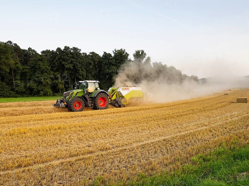 Farmer baling straw with his tractor and baler on a field after the corn harvest, the air above the landscape covered in dust from the dry straw, North Hesse, Germany, Europe