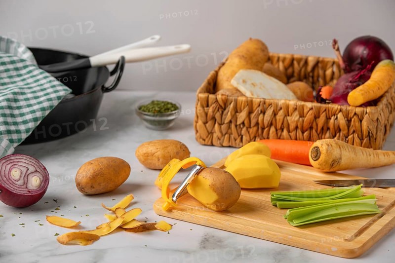 Peeled potatoes on a wooden board next to soup vegetables, preparation for cooking