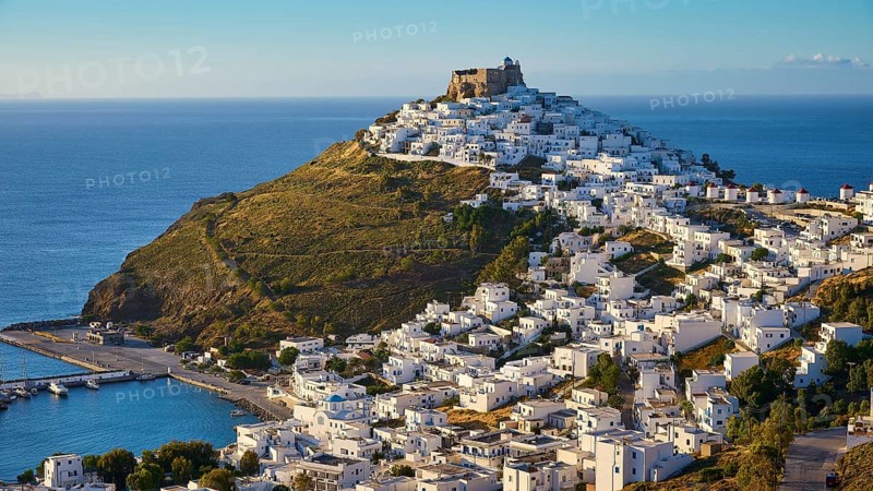 A fortress overlooks a coastal landscape of white houses gently sloping down to a blue sea, Querini Castle, harbour, Chora, Astypalea, Dodecanese, Greek Islands, Greece, Europe