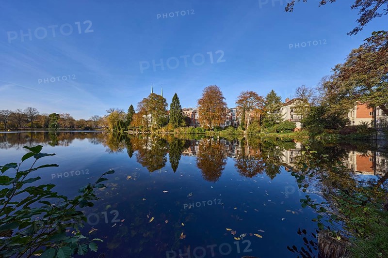 Mill pond with trees, general buildings against a cloudless blue sky, symmetrical reflections on the water surface, Hanseatic city of Lübeck, Schleswig-Holstein, Germany, Europe