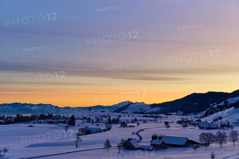 Snowy landscape at sunrise with mountains and farms, bathed in a warm orange-blue light, Menzingen, Zug, Canton Zug, Switzerland, Europe