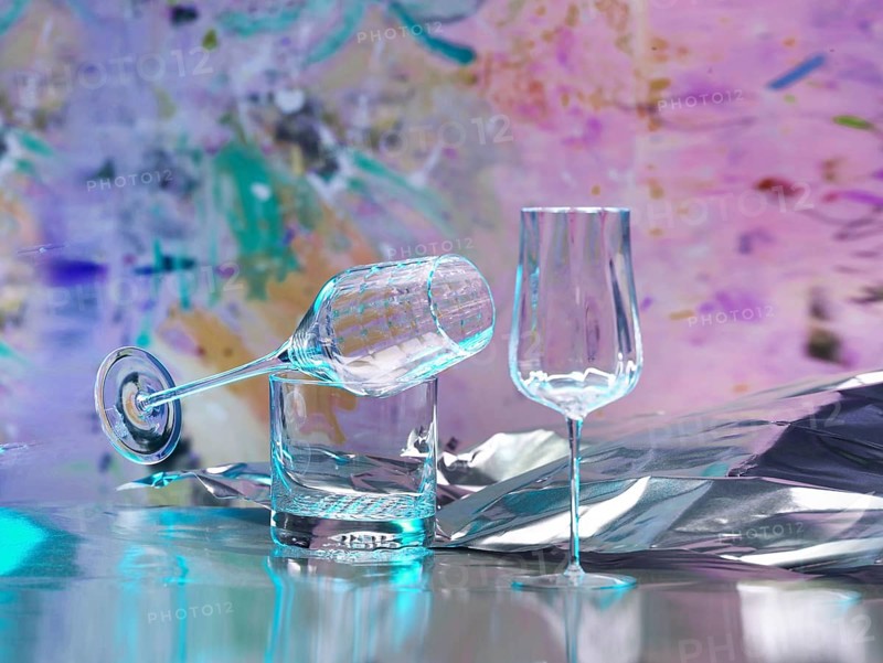 Various glasses on silver foil, behind them various splashes of colour, studio shot