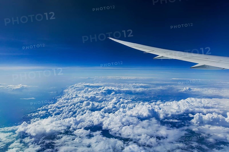 Above the clouds over the Indian Ocean. On the left, the coast of India. View from the aircraft window during a flight with the airline Etihad. Blue sky and cloud structures over the sea, wing of a Boeing 787 aircraft
