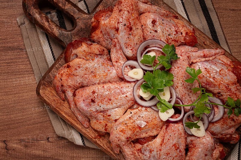 Chicken wings, marinated and laid out on a wooden platter, ready for cooking, grilling or baking, in a home kitchen, there are no people