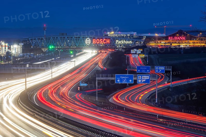 A8 motorway at Stuttgart Airport in the evening. Heavy traffic, lanes of light. Modern architecture of Messe Stuttgart with multi-storey car park above the motorway lanes. Logo of the Bosch company. Stuttgart, Baden-Württemberg, Germany, Europe