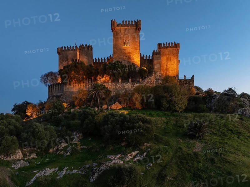 The impressive eighth-century Moorish castle of Almodóvar del Río perches high above the Guadalquivir river valley. Floodlit at dusk. Drone shot. Córdoba province, Andalusia, Spain, Europe