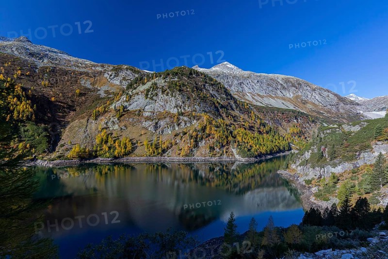 The Galgenbichl reservoir with a mountain forest in fall foliage on a bright sunny morning. Seen from the Malta Hochalm road. Carithia, Austria, Europe