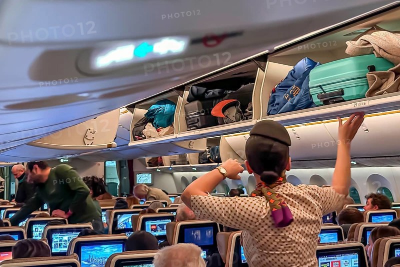 Etihad airline aircraft, interior, rows of seats with passengers. Boeing 787 aircraft on a flight to Munich. A flight attendant stows the luggage in the overhead compartment. Abu Dhabi, United Arab Emirates, UAE, Asia