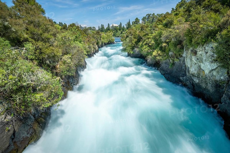 A rushing waterfall at Huka Falls surrounded by lush vegetation and blue sky, Taupo, New Zealand, Oceania