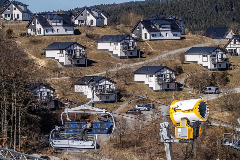 Winter sports area in the Sauerland, Winterberg ski lift carousel, artificial snow slopes, artificial snow from over 360 snow guns, Poppenberg ski area, 12 of 24 lifts are in operation in mid-March, the rest of the landscape is snow-free, in the background holiday homes at Landal Ferienpark Winterberg, North Rhine-Westphalia, Germany, Europe