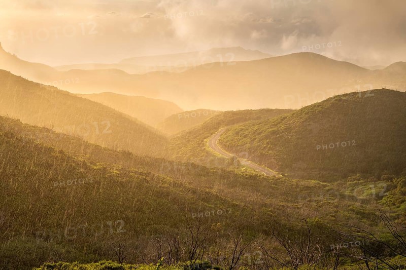 View from a path below the summit of Garajonay to other mountains of the Garajonay National Park and a road. Rain, sun and golden hour with bright clouds. Parque Nacional de Garajonay, La Gomera, Canary Islands, Spain, Europe
